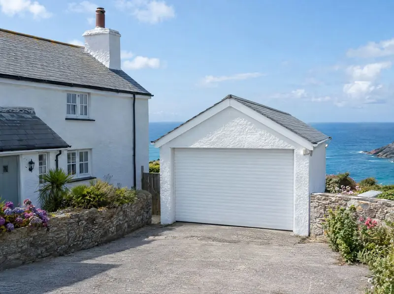 White roller garage door on a whitewashed coastal garage with the sea behind