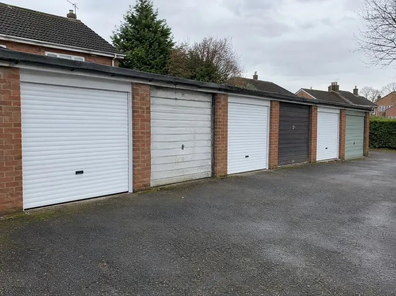 Row of lock-up garages with a mix of new white roller doors and old up-and-over doors