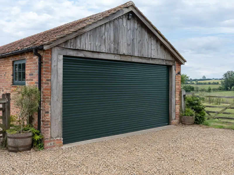 Wide dark green roller door on a brick and timber rural outbuilding beside fields